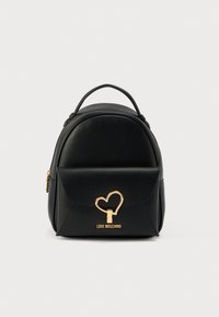 Μαύρο σακίδιο από συνθετικό δέρμα με στρογγυλεμένο σχήμα, μπροστινή τσέπη με καπάκι, χρυσά μεταλλικά στοιχεία σε σχήμα καρδιάς και λογότυπο της μάρκας στο κάτω μέρος.