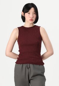 Top burgundiu fără mâneci, cu o suprafață texturată, design ajustat și guler rotund, asortat cu pantaloni gri, de tip lejer.