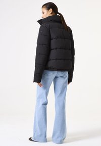 Schwarze Puffjacke mit hohem Kragen und steppendem Design, mit tailliertem Schnitt und langen Ärmeln, kombiniert mit hellblauen Schlagjeans.