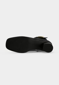 Chaussure à talon en cuir noir vue de la semelle avec une forme carrée à l'avant et une surface texturée sur la partie avant.