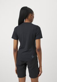 Svart treningst-shirt med korte ermer, laget av glatt materiale. Har en diskret logo nederst til venstre og matchende svarte shorts.
