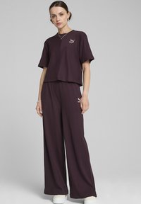 Paarse geribde crop top met korte mouwen en bijpassende brede broek, met een klein gouden logo op de borst en het linker broekbeen.