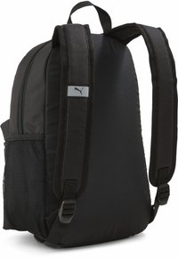 Mochila negra con correas de hombro acolchadas, un bolsillo lateral de malla y un pequeño logotipo gris de Puma en una correa. Textura de tela suave.