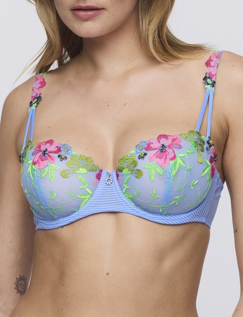 Sujetador azul bordado con patrones florales en rosa, verde y negro. Presenta tirantes ajustables y una gema decorativa en el centro.