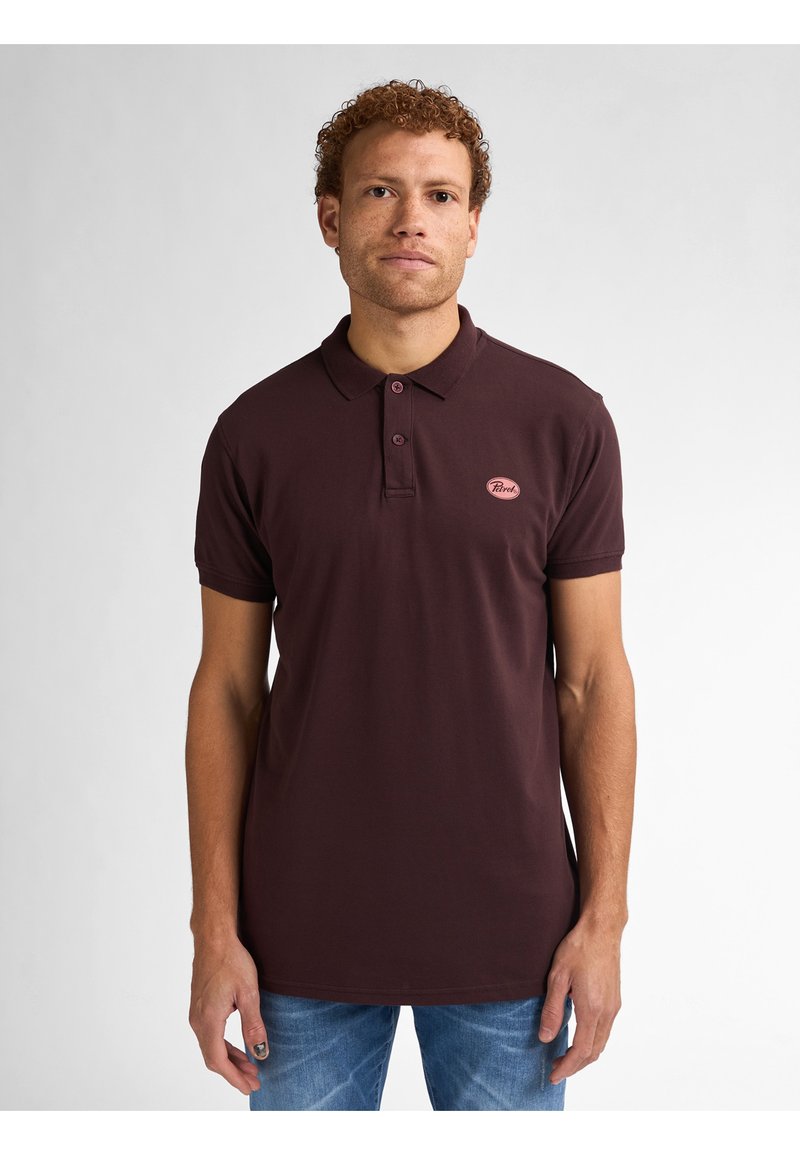 Bordowa koszulka polo wykonana z bawełny, z kołnierzykiem, zapinana na dwa guziki oraz małą łatką z logo na klatce piersiowej. Połączona z jasnymi dżinsami.