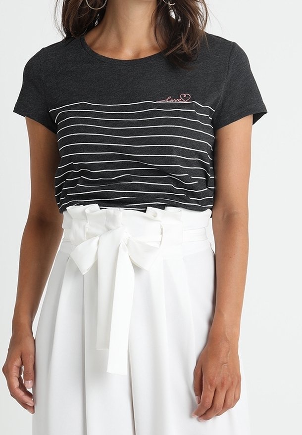 Kvinna som bär en svart och vit randig t-shirt med "love" brodyr och högmidjade vita byxor med en knytbälte.