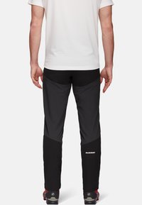 Zwarte outdoorbroeken met een slim fit, rekbare stof en contrasterende zijpanelen. Logodetail op het onderbeen, gecombineerd met wandelschoenen.