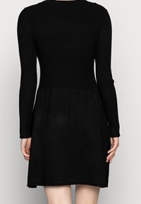 Robe noire tricotée à manches longues, avec un corsage côtelé et une jupe évasée, présentant une texture lisse et un design mi-long.
