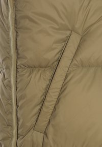 Olivgrüne Pufferjacke mit gesteppten Paneelen und einer Seitentasche. Der Stoff wirkt glatt und leicht glänzend, mit einem versteckten Reißverschluss.