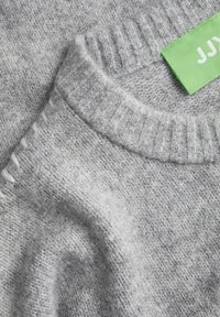 Pull en tricot gris avec un col rond côtelé. Présente un matériau texturé et doux ainsi qu'une étiquette de marque verte sur le col.