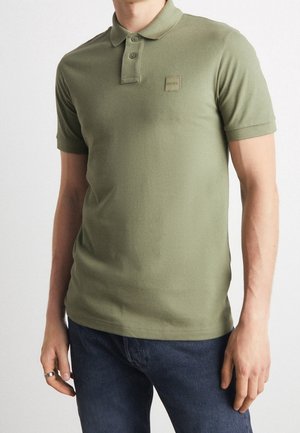 Polo verde oliva con colletto, placca con due bottoni e patch quadrato sul petto. Realizzato in tessuto morbido e liscio.
