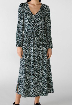 Robe à imprimé floral vert foncé avec manches longues, décolleté en V et fentes latérales. Confectionnée en tissu léger, elle présente de petites fleurs bleues et blanches.