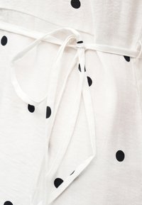 Λευκό ύφασμα με μαύρες πουά, με δέσιμο υφασμάτινης ζώνης ή ζωνάρι γύρω από την περιοχή της μέσης.