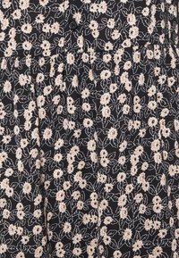 Tissu noir avec un motif floral composé de petites fleurs crème et de feuilles vertes, accentué par un design plissé et un détail de bouton.