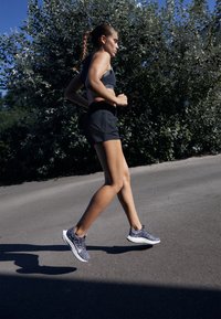 Hardloopschoenen met een gestructureerde donkerblauwe bovenkant, witte zolen; model in een zwart sportoutfit die jogt op een betonnen pad.
