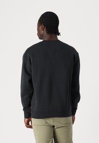 Μαύρη βαμβακερή ζακέτα με στρογγυλή λαιμόκοψη και ριμπ μανσέτες, σε χαλαρή γραμμή. Ο σχεδιασμός στην πλάτη είναι απλός και χωρίς στολίδια.