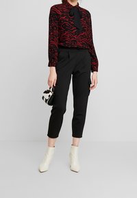 Camicia nera con motivo astratto rosso, pantaloni neri fitted con tasche cargo e stivali alla caviglia bianchi. Piccola borsa a tracolla nera e bianca.