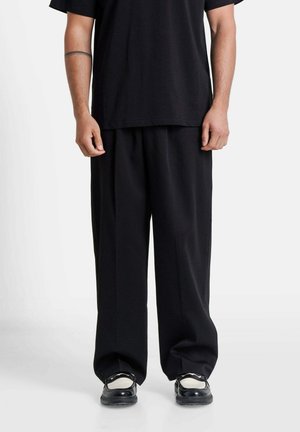 Zwarte soepelvallende broek van gladde stof, met een recht model en plooien, gecombineerd met een relax-fit zwart t-shirt en zwarte schoenen.