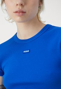 T-shirt blu a coste con scollatura rotonda e una piccola etichetta rettangolare "HUGO". Texture liscia e design aderente.