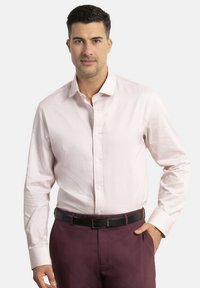 Camisa de botones de color rosa claro con un sutil patrón geométrico, mangas largas y cuello. Combinada con pantalones negro burdeos y un cinturón negro.