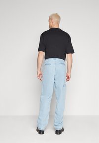 Un tricou din bumbac negru cu mâneci scurte, asociat cu o pereche de pantaloni din denim de un albastru deschis, cu buzunare și manșete elastice. Încălțăminte neagră.