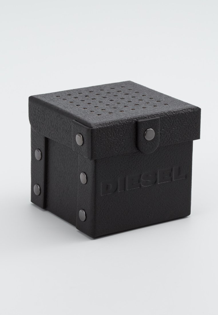 Caja cuadrada negra hecha de un material texturizado, con orificios de ventilación en la tapa, acentos metálicos y la palabra "DIESEL" en relieve en el lateral.