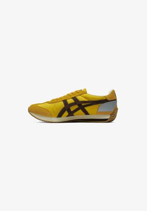 Gule sneakers med brune accenter, lavet af ruskind og syntetiske materialer, tekstureret sål og klassisk snøredesign. Har sølvdetaljer ved hælen.
