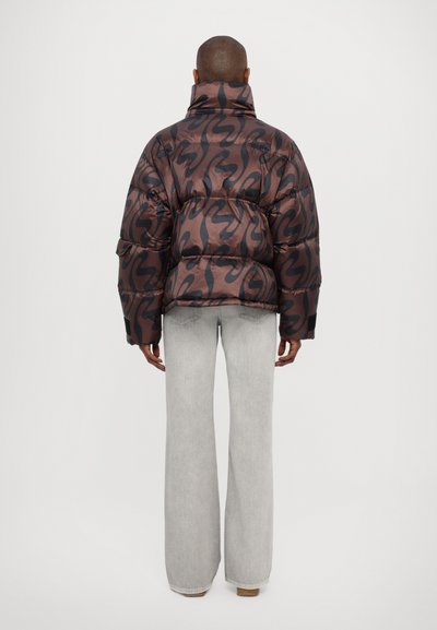 Puffer jacket in brown with a black abstract pattern, featuring a high collar and wide sleeves. Paired with light grey flared pants.