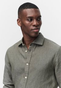 Lichtgroen linnen shirt met een button-down kraag, voorzien van een knopenlijst aan de voorkant en subtiele textuur, gedragen door een persoon die uit het frame kijkt.