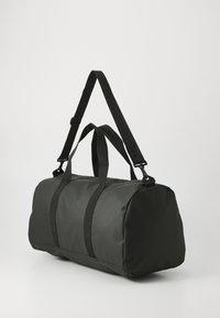Sac de voyage en nylon noir mat, doté de deux poignées supérieures et d'une bandoulière réglable. Forme arrondie avec une texture lisse.