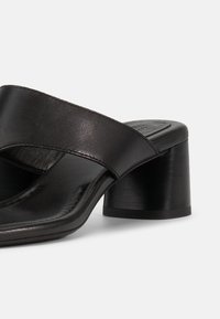 Μαύρο mule σανδάλι από δέρμα με φαρδιές σταυρωτές λωρίδες και χαμηλό, χοντρό τακούνι, σε λευκό φόντο.