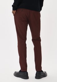 Pantalones burdeos de corte slim, hechos de una tela texturizada. Cuentan con bolsillos traseros con botones y puños enrollados, combinados con mocasines negros.