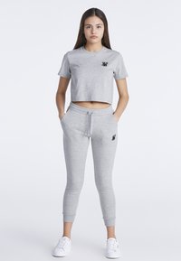 Camiseta gris de corte corto con mangas cortas, con un logo negro; combinada con pantalones elásticos grises a juego y zapatillas blancas.