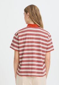 Polo rayé en rouge, crème et bleu marine. Manches courtes, tissu texturé, col uni, coupe décontractée avec fentes latérales.