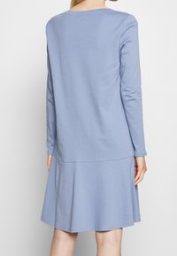 Långärmad klänning i ljusblå bomull, med en utsvängd nederdel och slät struktur, samt en enkel, rundad halsringning.