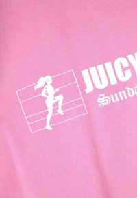 Rozā kokvilnas T-krekls ar baltu grafiku, kurā attēlots skrienošs cilvēks un teksts "JUICY Sunday" biezā fontā. Gluda tekstūra.