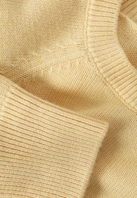 Tissu de pull tricoté jaune clair avec un col et des poignets côtelés, une texture lisse et des détails de coutures visibles.