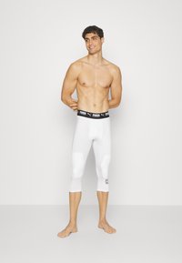Hvide træningsleggings med knælængde, sort elastisk talje med Puma-logo, og subtile detaljer nederst på benet.