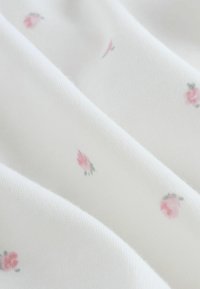 Fehér pamutszövet finom virágmintával, apró rózsaszín rózsákkal, zöld kontúrral, lágy textúrával és sima hajtásokkal.