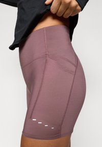 Shorts taille haute et ajustés en mauve avec des coutures apparentes et un détail accent blanc sur la jambe. Fabriqués en tissu extensible.