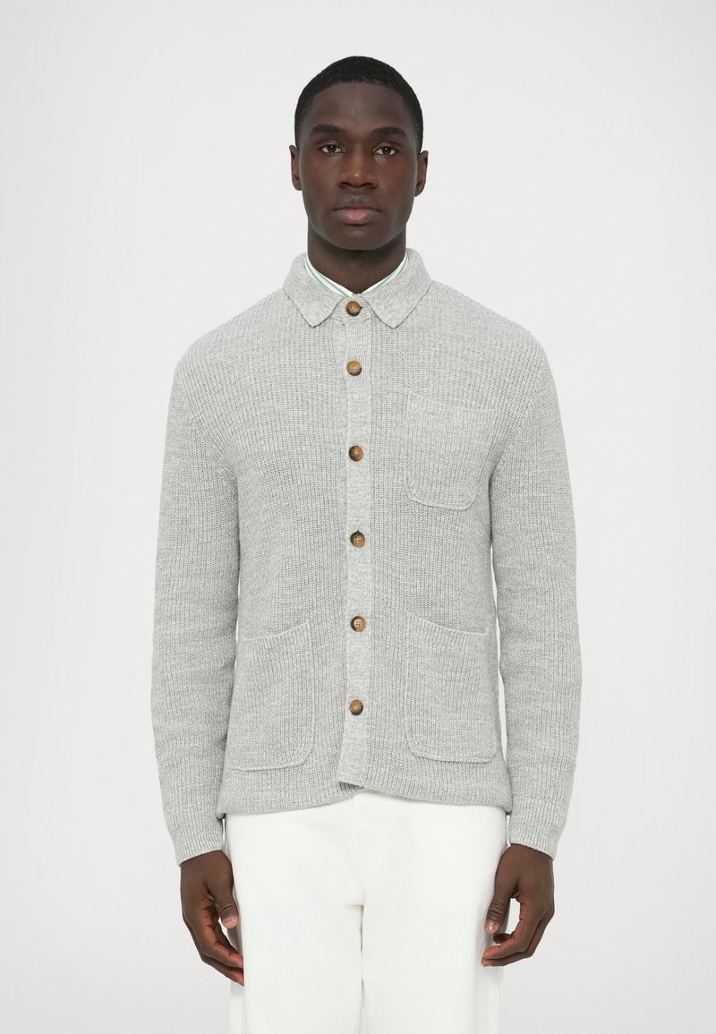 Pilka megzta kardiganas su sagomis priekyje, mediniais mygtukais, dviem priekinėmis kišenėmis ir apykakle, pagamintas iš tekstūruotos medžiagos.