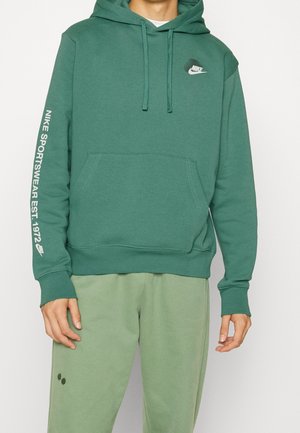 Haut à capuche Nike vert avec une poche avant, capuche à cordon de serrage et logo sur la poitrine. Présente un texte blanc le long de la manche gauche. Tissu doux et texturé.