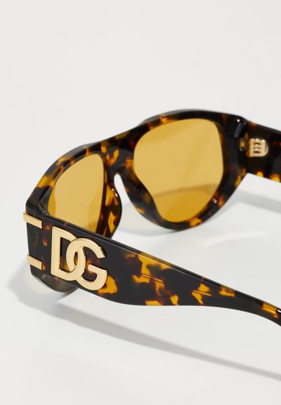 Ochelari de soare cu model țestoasă, cu accente aurii, prezentând un logo 'DG' îndrăzneț pe braț și lentile galbene. Finisaj neted și lucios.
