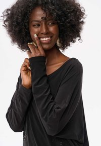 Schwarzes Langarmoberteil mit lockerer Passform, V-Ausschnitt und strukturierten Details. Der Stoff wirkt weich und leicht drapiert.
