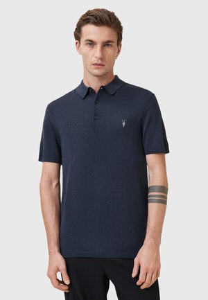 Mørkeblå polo shirt lavet af blødt stof, med en klassisk krave, tre knapper og et lille broderet logo på venstre bryst.