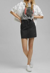 Zwarte denim minirok met rafelige zoom; gecombineerd met een grijs graphic t-shirt. Witte denimjas en witte sneakers maken de outfit compleet.