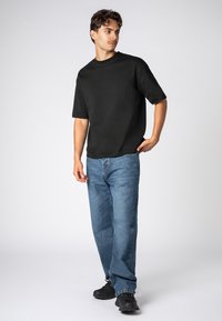 Schwarzes Kurzarm-T-Shirt kombiniert mit hellblauen, geraden Jeans und schwarzen Sneakern. Das T-Shirt hat eine schlichte Textur und einen lockeren Schnitt.