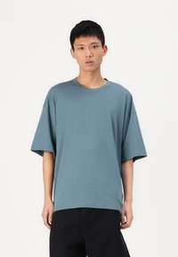 Laza szabású, rövid ujjú póló, tompa türkiz színben, puha pamut anyagból készült, kerek nyakú és egyenes aljjal rendelkezik.