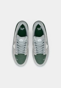 Adidași Nike SB cu un superior din suede gri și accente din piele verde, bot perforat, șireturi plate gri și talpă albă.