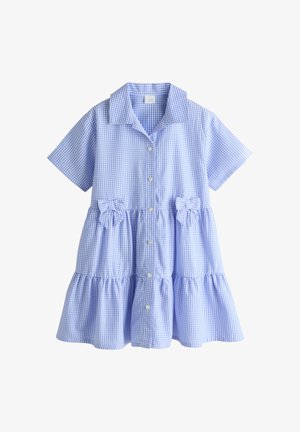 Primo piano del braccio di una persona che indossa un vestito a quadri blu e bianco con maniche corte e un fiocco abbinato in vita.